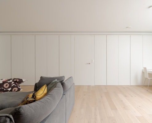 Un salon moderne avec un canapé gris et un mur blanc sans décorations visibles.