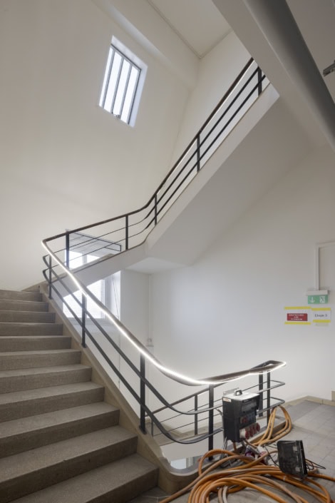Escalier intérieur moderne avec rampe en métal, éclairage LED, espace lumineux et épuré.