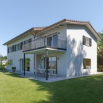 Maison moderne à deux étages avec balcon et espace extérieur en gazon.
