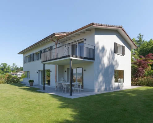 Maison moderne à deux étages avec balcon et espace extérieur en gazon.