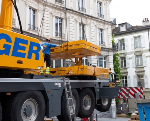 Opérateur de grue en train de soulever une charge sur un chantier de construction en milieu urbain.