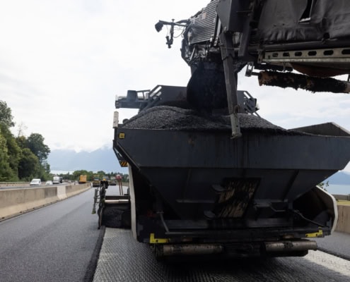 Camion de construction déversant de l'asphalte sur une route en cours de réparation.