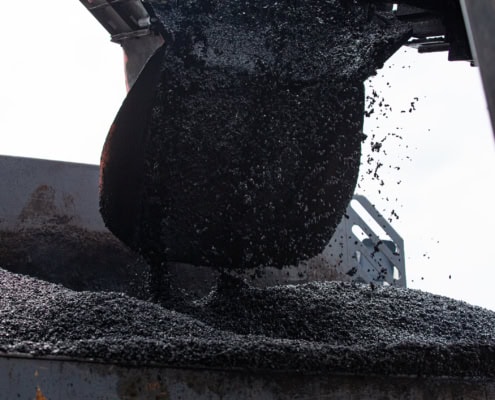Un seau déversant de l'asphalte noir sur une surface lors d'un processus de construction.