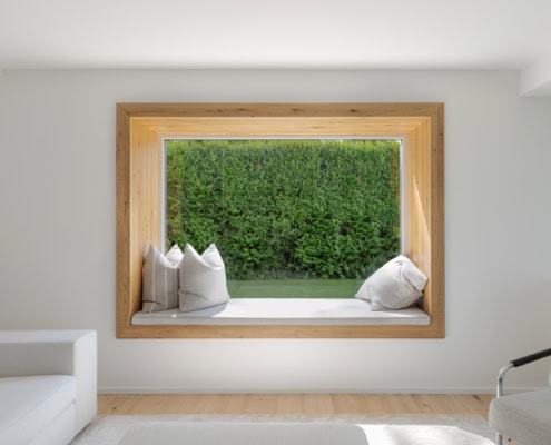 Fenêtre encadrée en bois avec un banc et des coussins à l'intérieur d'une pièce.