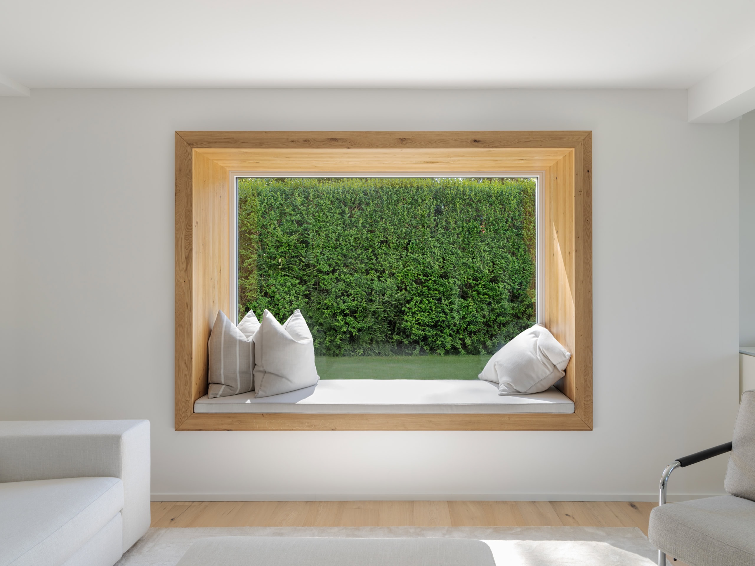 Fenêtre encadrée en bois avec un banc et des coussins à l'intérieur d'une pièce.