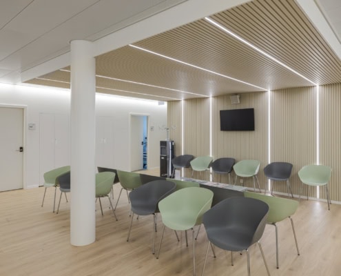 Salle d'attente avec des chaises en plastique de différentes couleurs et un mur en bois à l'arrière.