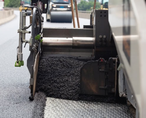 Machine de pavage d'asphalte appliquant une couche d'asphalte sur une route en construction.