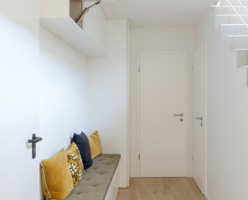 Banc en bois avec coussins noirs et jaunes dans un couloir lumineux et minimaliste.