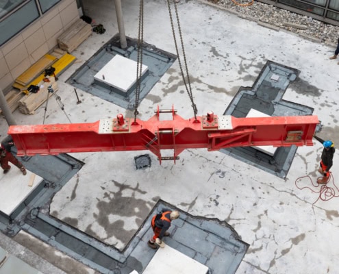 Grue rouge suspendue au-dessus d'un chantier de construction avec des travailleurs en bas.