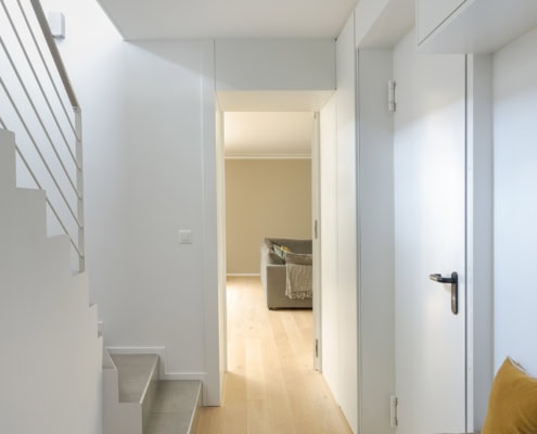 Couloir moderne avec un escalier, un mur blanc et un banc avec un coussin jaune.
