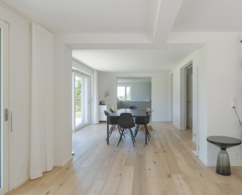 Intérieur d'une maison moderne avec une salle à manger et des fenêtres lumineuses.