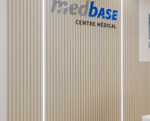 Panneau en relief avec le texte 'medbase centre médical' sur un mur à l'intérieur d'un espace médical.