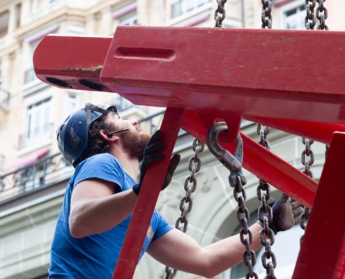 Un ouvrier portant un casque et des gants, regardant un équipement de levage rouge en métal.