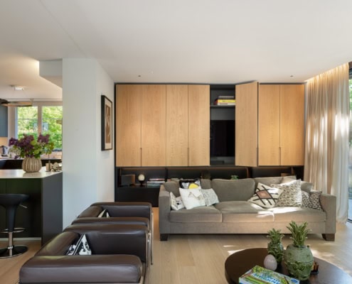Un salon moderne avec un canapé beige, des fauteuils en cuir et un meuble en bois clair sur le mur.
