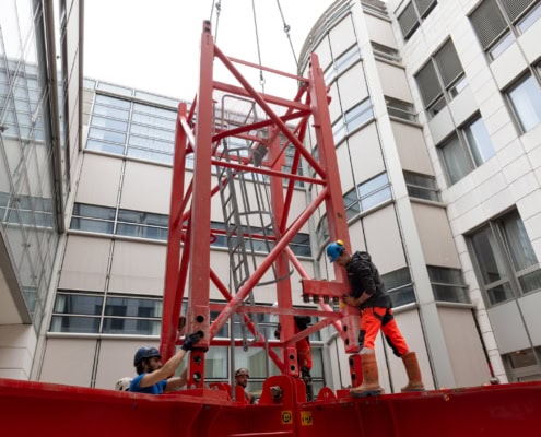 Deux travailleurs en train d'installer une structure de levage rouge dans un espace intérieur.