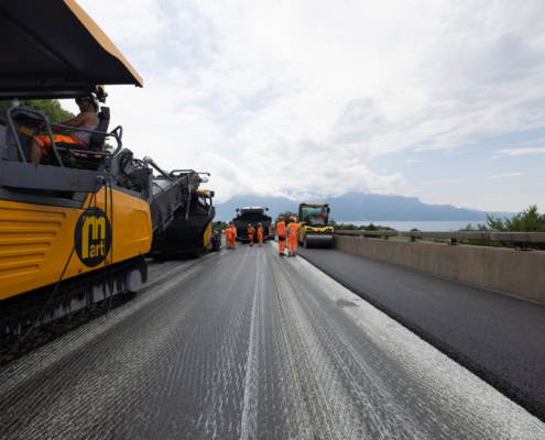 Équipe de travailleurs en orange utilisant des machines sur une route en cours de construction.