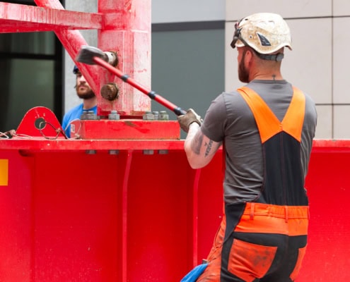 Ouvrier en vêtements de sécurité utilisant un marteau sur un équipement de construction rouge.