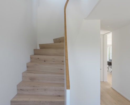 Escalier en bois clair avec une rampe blanche dans un intérieur moderne.