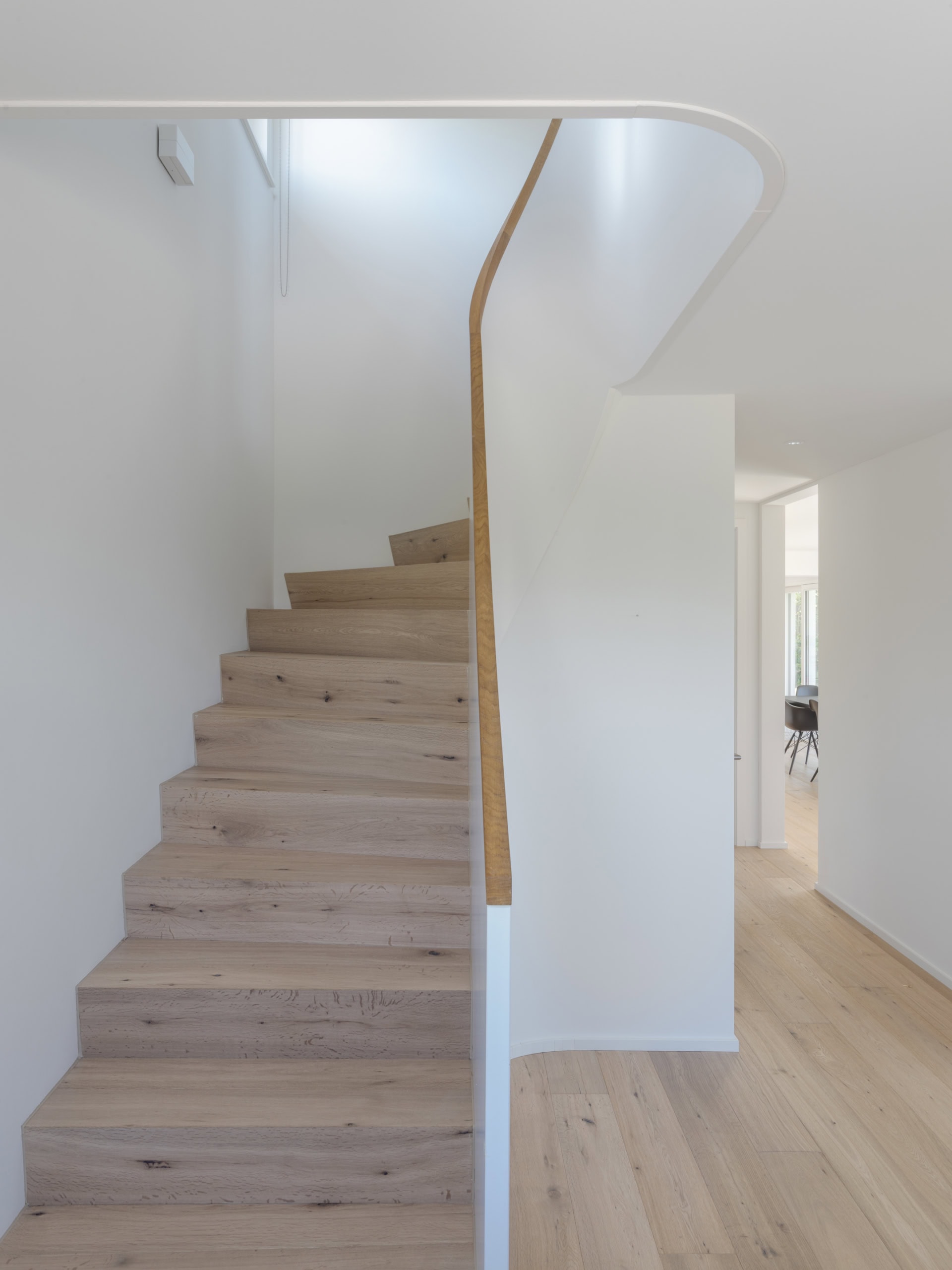 Escalier en bois clair avec une rampe blanche dans un intérieur moderne.
