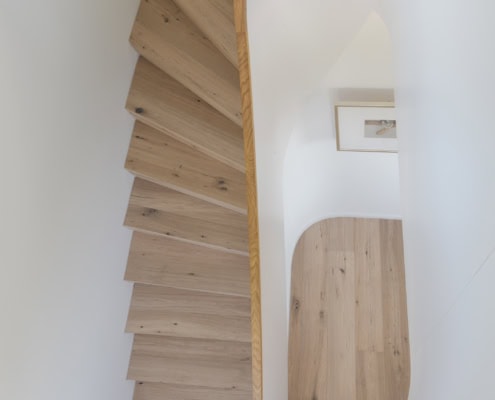Escalier en bois clair avec une rampe courbée, vu d'un angle supérieur.