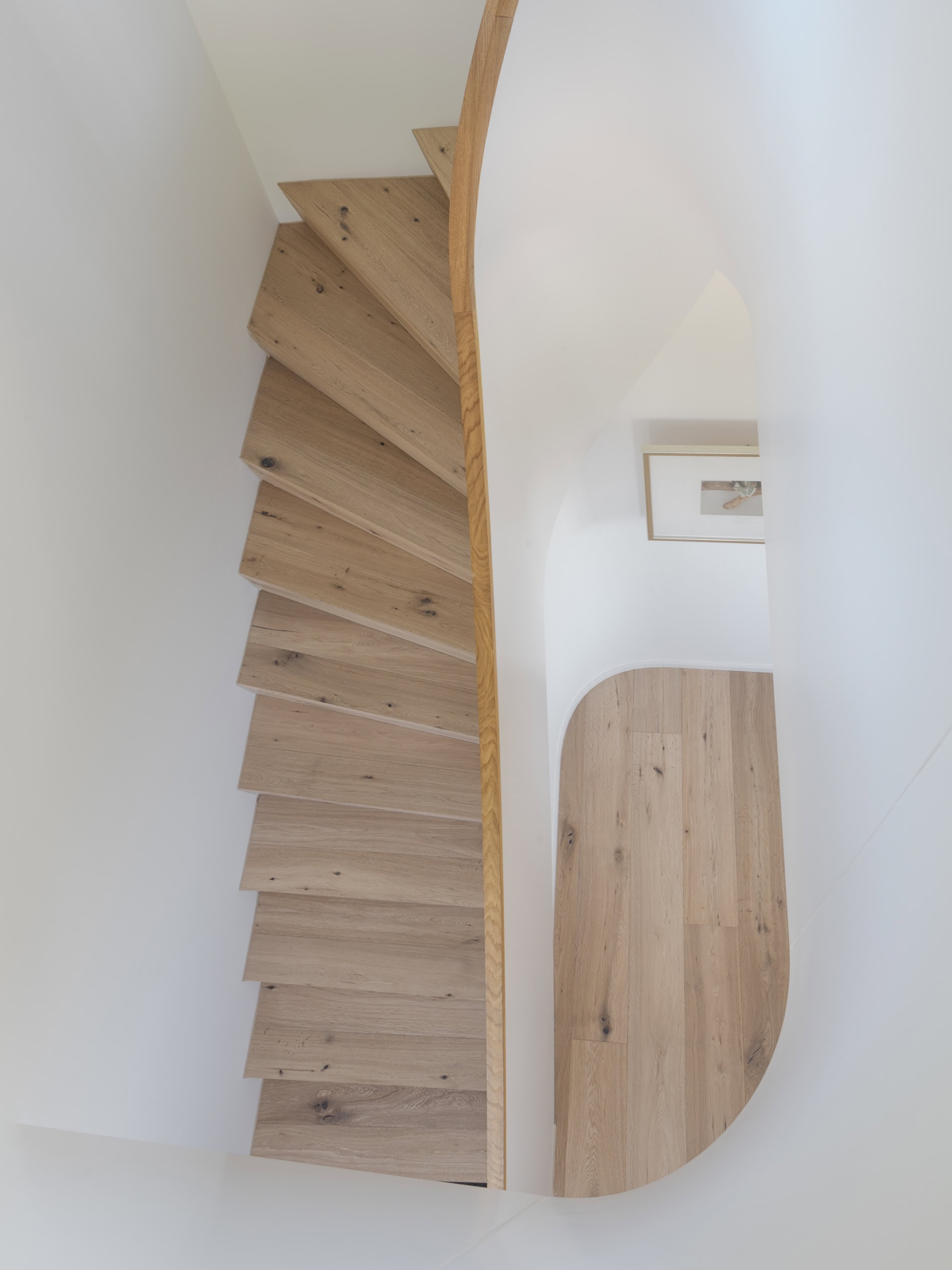 Escalier en bois clair avec une rampe courbée, vu d'un angle supérieur.