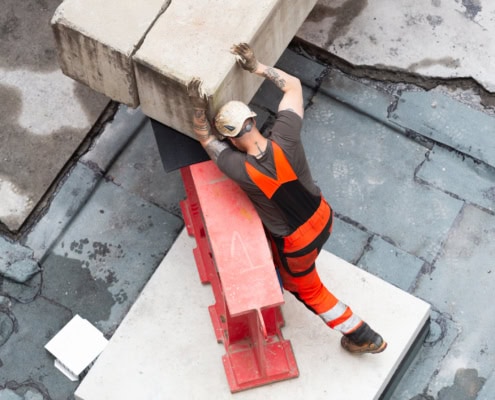 Un ouvrier de construction en vêtements de sécurité manipulant un bloc de béton sur un chantier.