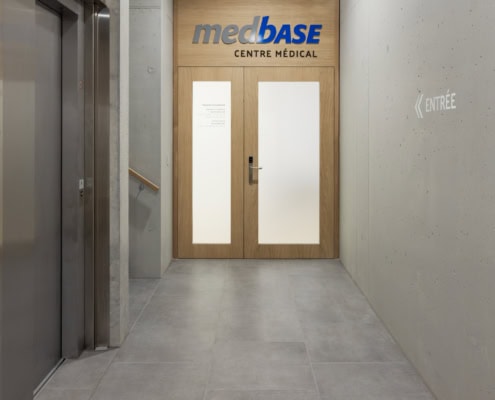 Porte d'entrée du centre médical Medbase avec un panneau indiquant 'entrée'.