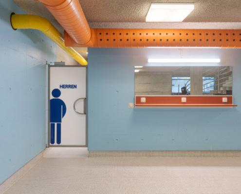 Porte des toilettes pour hommes avec un symbole masculin sur un mur bleu dans un espace intérieur.
