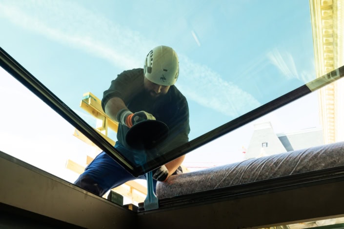 Travailleur posant du verre isolant sous un ciel bleu en construction, professionnel à Lausanne.