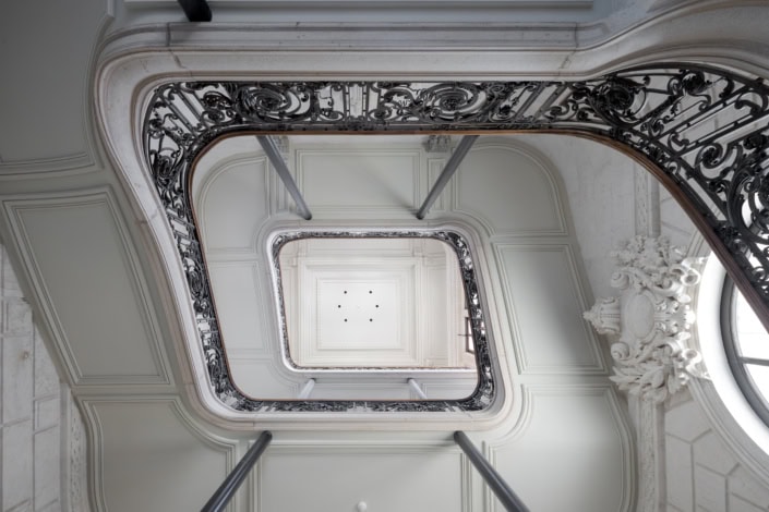 Escalier intérieur élégant avec balustrade en fer forgé et plafond orné de moulures.