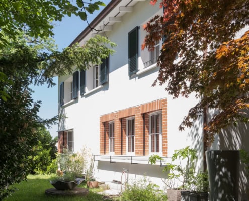 Maison blanche avec fenêtres à volets verts et jardin verdoyant à l'extérieur.