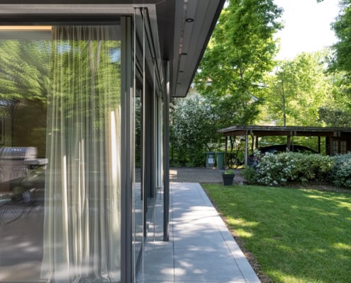 Vue d'un coin d'une maison moderne avec de grandes fenêtres en verre et un jardin verdoyant.