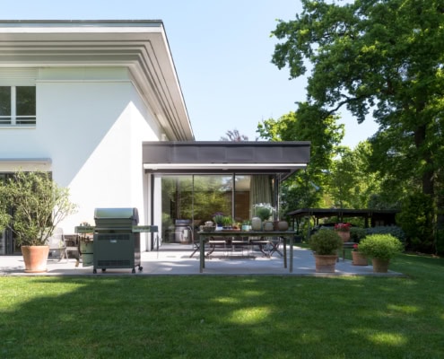 Terrasse d'une maison moderne avec mobilier en extérieur et barbecue, entourée de verdure.