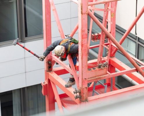 Un ouvrier en train de travailler sur une grue rouge, utilisant un outil pour effectuer des tâches de construction.