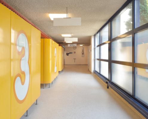 Couloir avec des casiers jaunes numérotés de 1 à 3 et des fenêtres laissant passer la lumière.