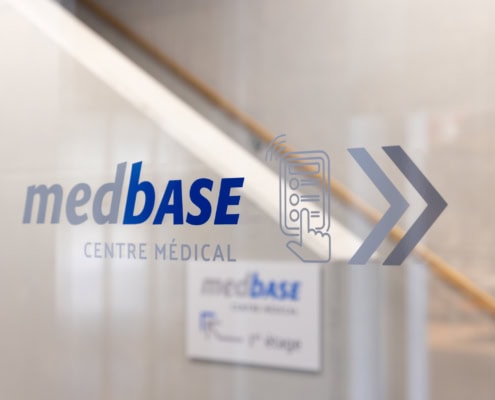 Logo de Medbase Centre Médical affiché sur une vitre avec un symbole de flèche.
