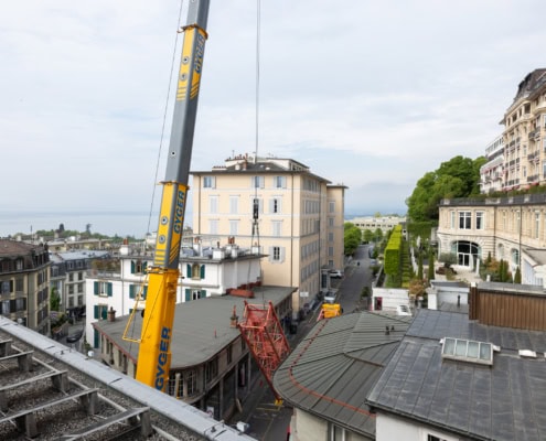 Grue de construction jaune sur un bâtiment avec vue sur un lac et des maisons environnantes.