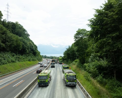 Camions de service verts circulant sur une route à plusieurs voies entourée d'arbres.