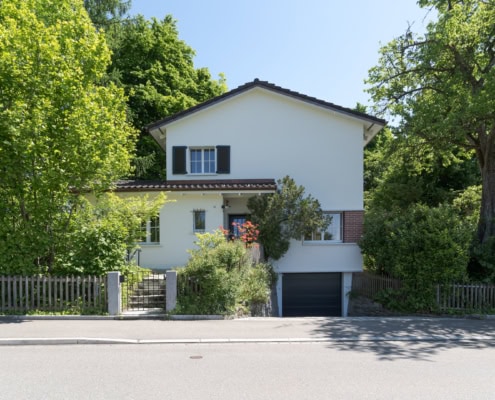 Maison à deux étages avec un jardin verdoyant et une entrée en escalier.