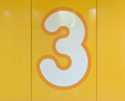 Panneau jaune affichant le chiffre trois en blanc, avec un design simple et moderne.