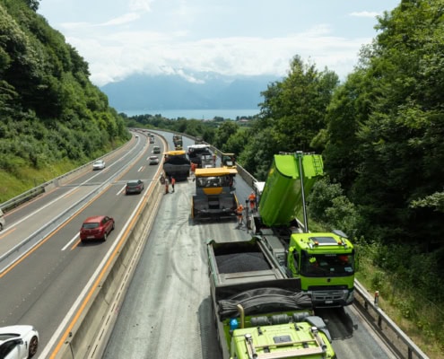 Des machines de construction effectuant des travaux sur une route avec des véhicules en circulation à proximité.