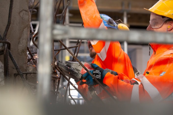 Travailleurs en uniforme orange utilisant un outil pour couper des ferrailles dans un chantier.