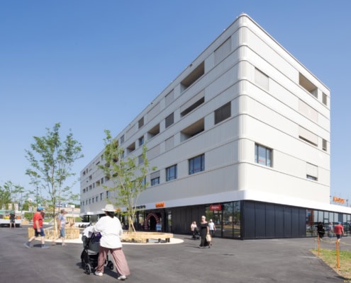 Immeuble moderne à plusieurs étages avec une façade blanche et des arbres plantés autour.