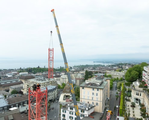 Grue rouge et grise en train de soulever des matériaux sur un bâtiment en construction dans une ville.
