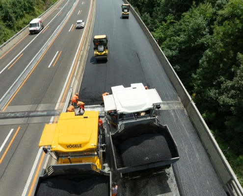 Engins de chantier en train de bitumer une route avec des ouvriers sur le site.