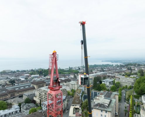 Grue rouge et grue mobile sur un chantier avec vue sur la ville et le lac en arrière-plan.