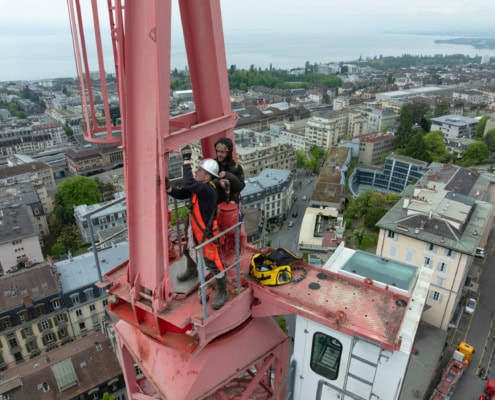 Deux travailleurs en tenue de sécurité sur une grue rouge, effectuant des ajustements en hauteur.