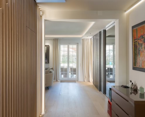 Un couloir moderne avec un meuble de rangement et des murs en bois, menant à une pièce lumineuse.