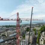 Grue rouge sur un chantier de construction avec vue sur la ville de Lausanne et le lac en arrière-plan.