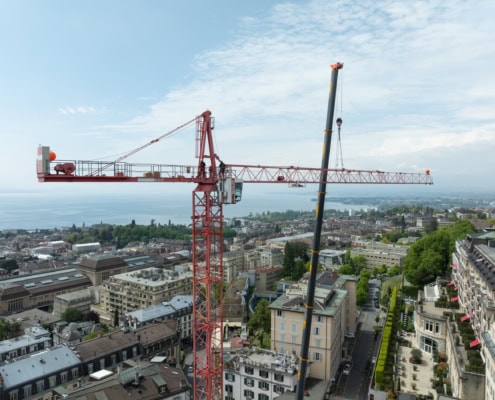 Grue rouge sur un chantier de construction avec vue sur la ville de Lausanne et le lac en arrière-plan.